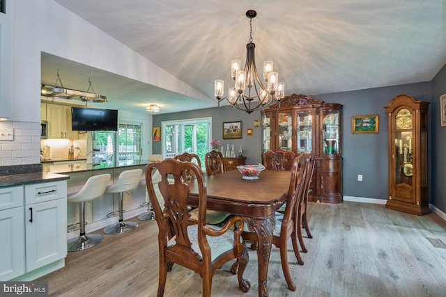 dining room featuring light wood-type flooring, a chandelier, and baseboards