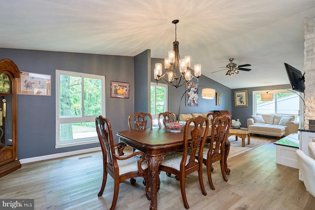 dining area featuring light wood-style flooring, a chandelier, lofted ceiling, a ceiling fan, and baseboards
