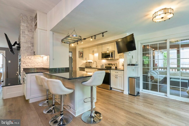 kitchen featuring stainless steel appliances, a peninsula, tasteful backsplash, light wood-style flooring, and white cabinets