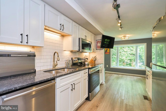 kitchen with stainless steel appliances, a sink, white cabinets, light wood finished floors, and dark stone countertops