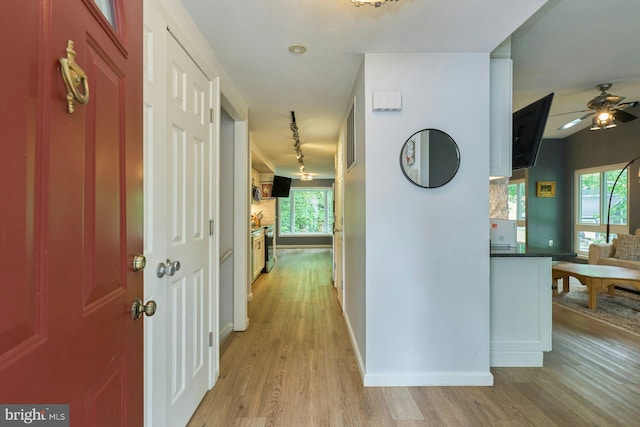 corridor featuring light wood-type flooring, baseboards, and healthy amount of natural light