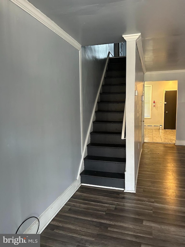 stairs featuring wood finished floors, ornamental molding, a baseboard heating unit, and baseboards