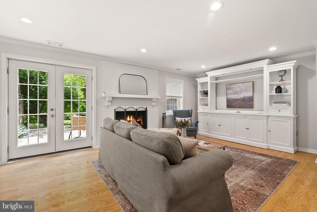 living room featuring crown molding, plenty of natural light, french doors, a brick fireplace, and light wood-style flooring