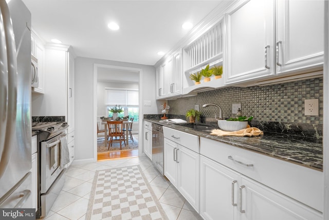 kitchen with appliances with stainless steel finishes, light tile patterned flooring, a sink, decorative backsplash, and dark stone countertops