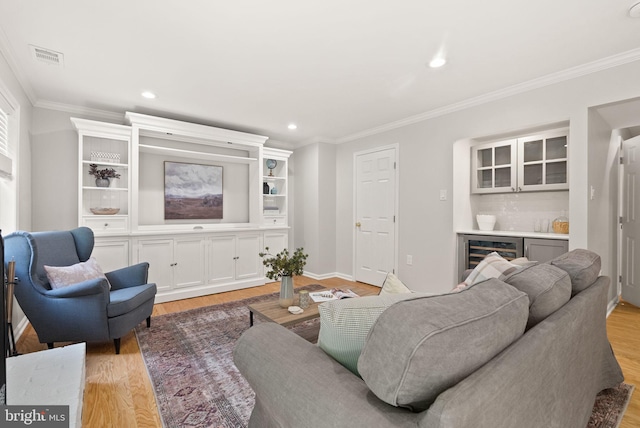 living room featuring beverage cooler, light wood finished floors, a dry bar, ornamental molding, and recessed lighting