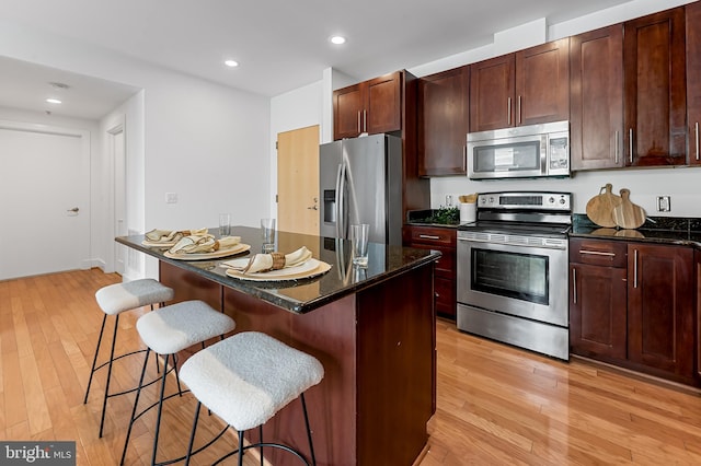 kitchen with stainless steel appliances, light wood-style flooring, a kitchen bar, a center island, and dark stone counters