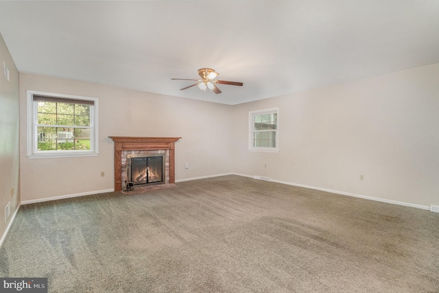 unfurnished living room with a ceiling fan, plenty of natural light, carpet, and a fireplace with flush hearth