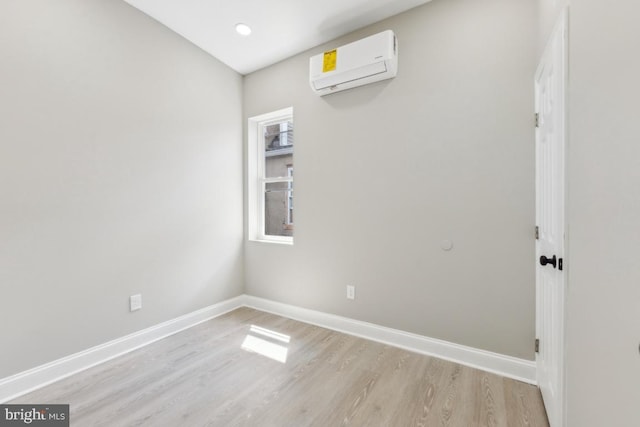 spare room featuring a wall unit AC, light wood-style flooring, and baseboards
