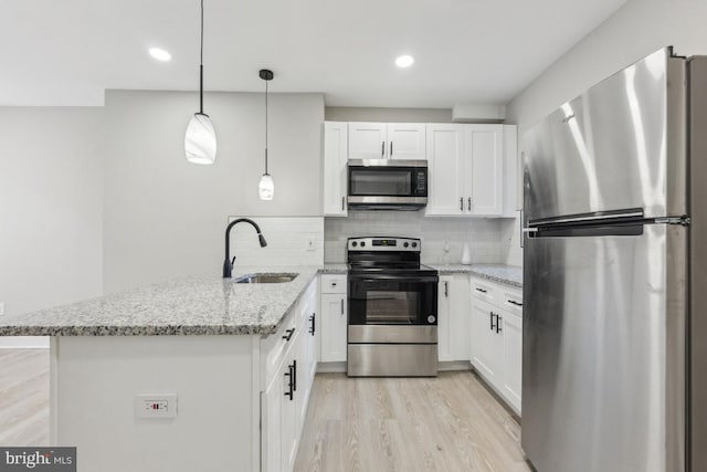 kitchen featuring appliances with stainless steel finishes, a peninsula, a sink, white cabinets, and light wood finished floors
