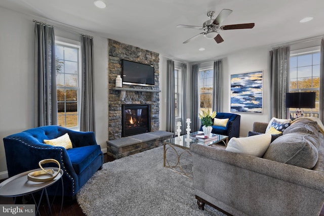 living room with wood finished floors, plenty of natural light, a stone fireplace, a ceiling fan, and recessed lighting