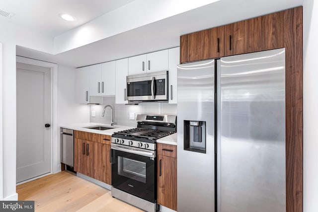kitchen featuring appliances with stainless steel finishes, a sink, light countertops, light wood-type flooring, and backsplash