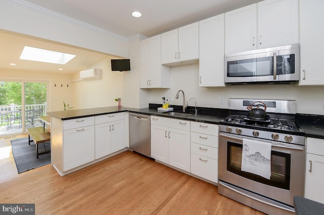 kitchen with appliances with stainless steel finishes, a sink, a skylight, a peninsula, and white cabinetry