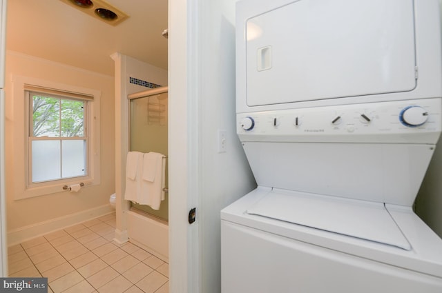 washroom with estacked washer and dryer, light tile patterned floors, and baseboards
