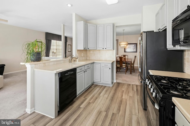 kitchen featuring black appliances, a sink, light wood-style flooring, backsplash, and light countertops