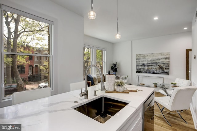 kitchen featuring a sink, light stone countertops, hanging light fixtures, dishwasher, and light wood-style flooring