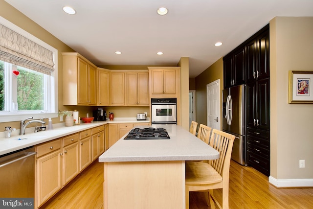 8931 Kiger St, Lorton, VA 22079 - kitchen featuring appliances with stainless steel finishes, light brown cabinets, a sink, a kitchen bar, and light wood-style floors