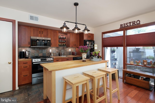 kitchen with appliances with stainless steel finishes, butcher block counters, tasteful backsplash, a kitchen bar, and hanging light fixtures