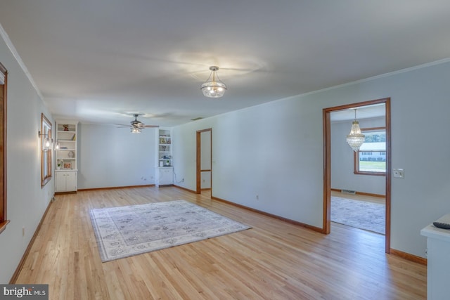 unfurnished living room featuring light wood-type flooring, ceiling fan, built in shelves, baseboards, and ornamental molding
