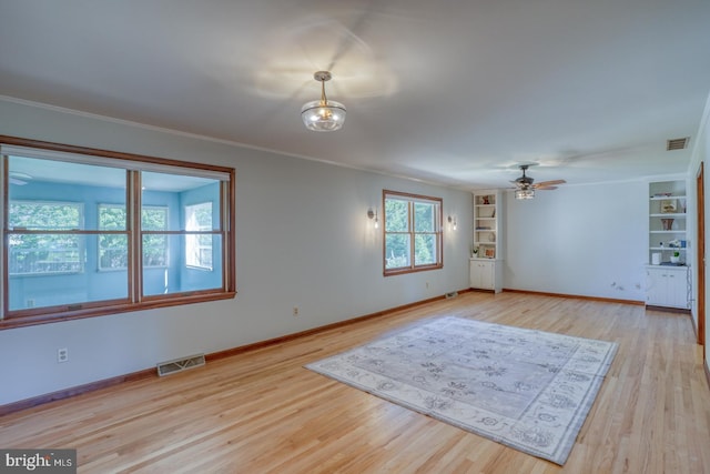 unfurnished room featuring light wood finished floors, baseboards, built in shelves, ceiling fan, and ornamental molding