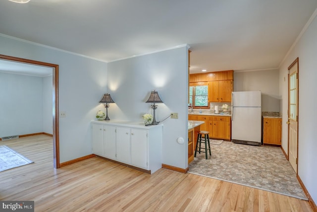 kitchen featuring freestanding refrigerator, light wood-type flooring, light countertops, ornamental molding, and a sink