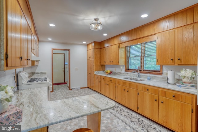 kitchen featuring white gas stove, a sink, under cabinet range hood, recessed lighting, and a peninsula