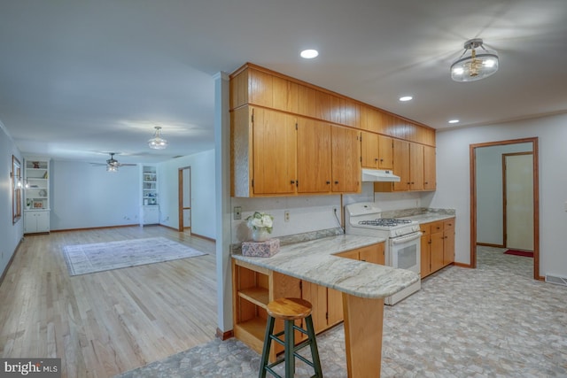 kitchen featuring white range with gas stovetop, under cabinet range hood, baseboards, light wood finished floors, and recessed lighting