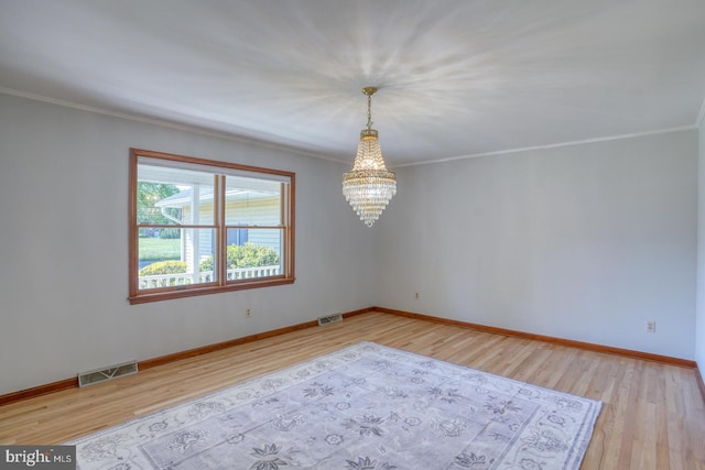 spare room with a chandelier, wood finished floors, ornamental molding, and baseboards