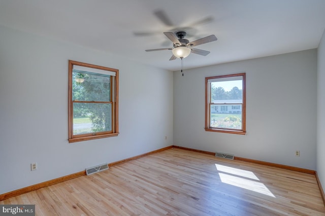 empty room featuring healthy amount of natural light, wood finished floors, ceiling fan, and baseboards