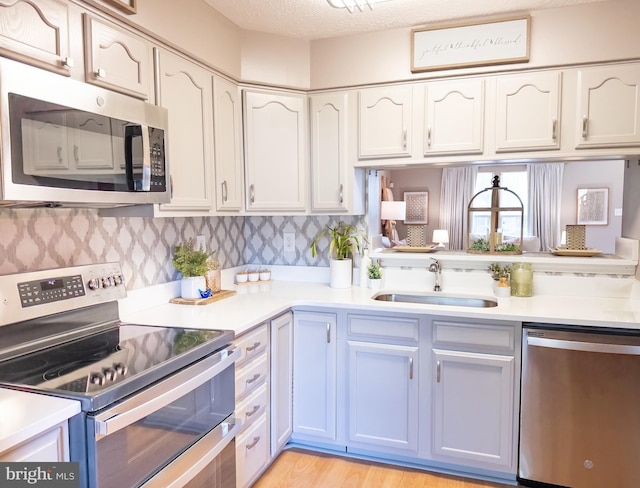 kitchen featuring stainless steel appliances, a sink, light countertops, and light wood-type flooring