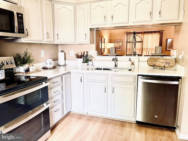 kitchen featuring appliances with stainless steel finishes, a sink, light countertops, and light wood-style flooring