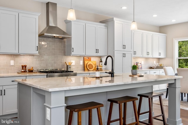 kitchen featuring wall chimney exhaust hood, a sink, stove, backsplash, and light stone counters
