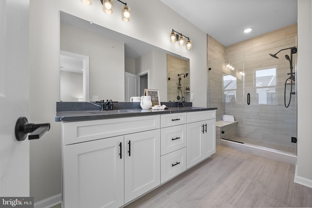 bathroom featuring a shower stall, double vanity, and baseboards