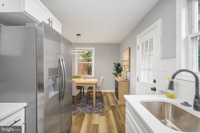 3531 Milford Mill Rd, Baltimore, MD 21244 - kitchen with stainless steel fridge, a sink, light wood finished floors, white cabinets, and hanging light fixtures