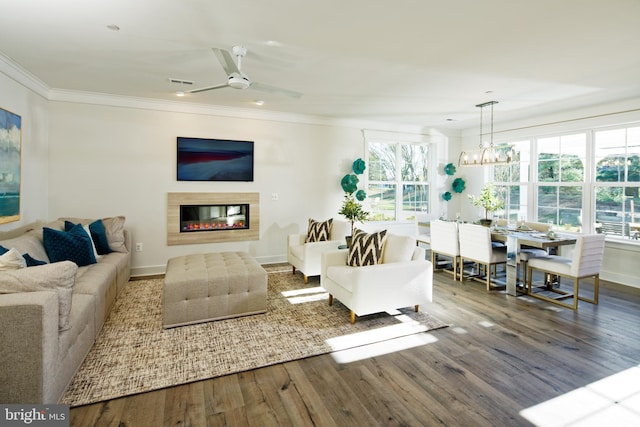 living area featuring wood finished floors, crown molding, a glass covered fireplace, baseboards, and a chandelier