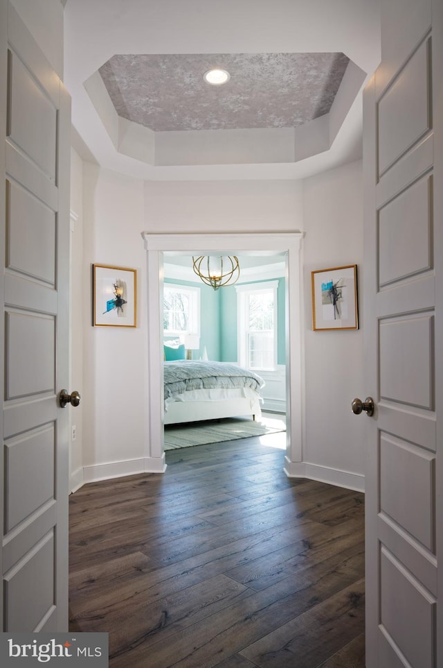 hall with a tray ceiling, baseboards, dark wood finished floors, and a chandelier