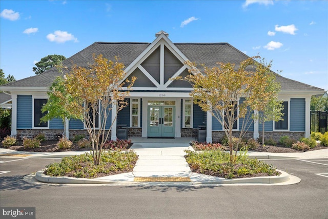 view of front of house with french doors, stone siding, covered porch, and a shingled roof