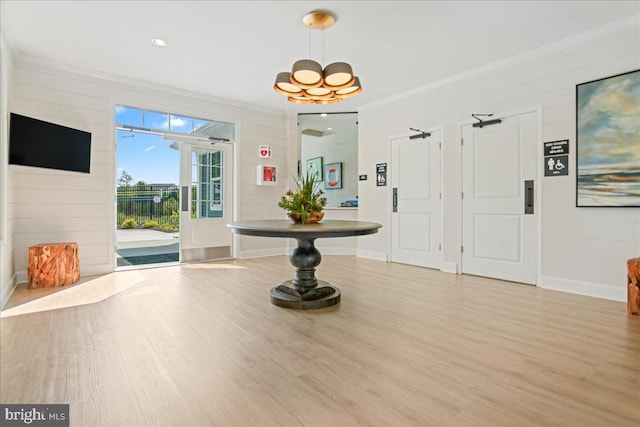 foyer entrance with ornamental molding, light wood-style flooring, wooden walls, baseboards, and a chandelier