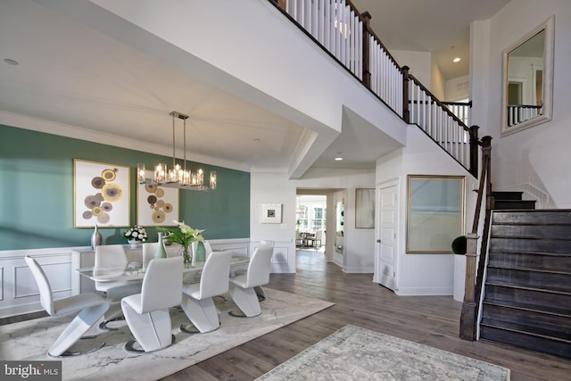 dining area with stairway, a chandelier, wood finished floors, a wainscoted wall, and ornamental molding