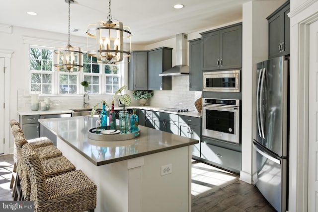 kitchen with stainless steel appliances, wall chimney exhaust hood, a chandelier, a sink, and a breakfast bar area