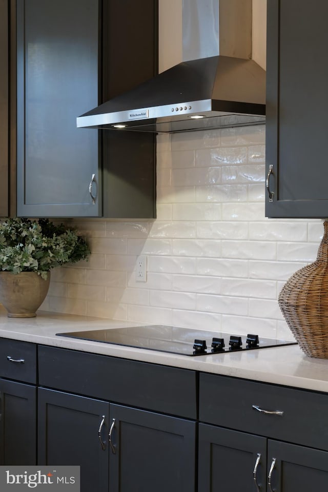 kitchen view of wall chimney range hood, gray cabinetry, tasteful backsplash, and light countertops