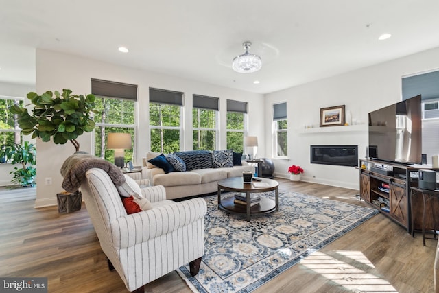living area featuring baseboards, wood finished floors, a glass covered fireplace, recessed lighting, and a chandelier