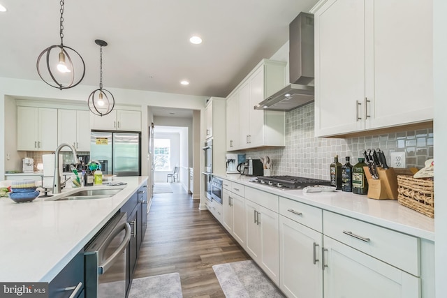 kitchen featuring appliances with stainless steel finishes, a sink, wall chimney exhaust hood, light countertops, and recessed lighting
