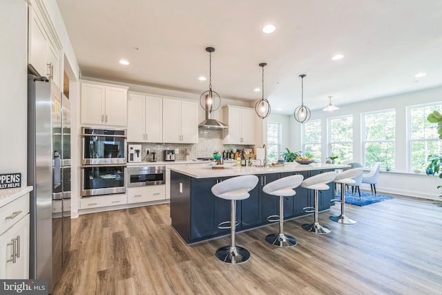 kitchen featuring appliances with stainless steel finishes, healthy amount of natural light, light countertops, an island with sink, and recessed lighting
