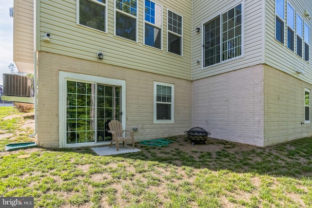 rear view of house with an outdoor fire pit, cooling unit, brick siding, and a lawn