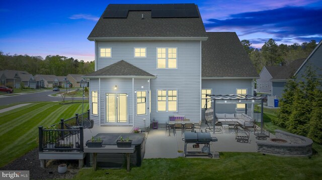 22378 Mahogany Rd, Milton, DE 19968 - back of property at dusk with a fire pit, a lawn, a patio, roof mounted solar panels, and roof with shingles