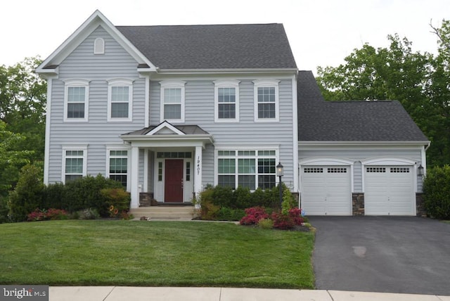 colonial home with a garage, asphalt driveway, a front yard, and roof with shingles