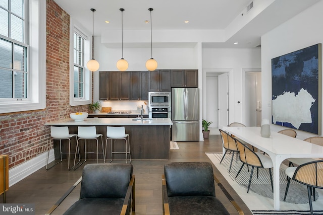 kitchen with appliances with stainless steel finishes, dark wood finished floors, dark brown cabinetry, light countertops, and a towering ceiling