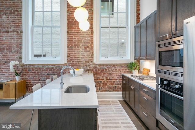 kitchen with stainless steel appliances, a sink, brick wall, healthy amount of natural light, and dark brown cabinetry