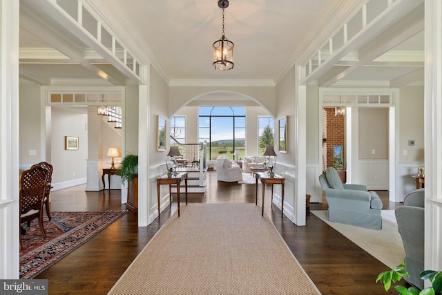 foyer entrance featuring crown molding, stairs, arched walkways, a decorative wall, and dark wood-style flooring