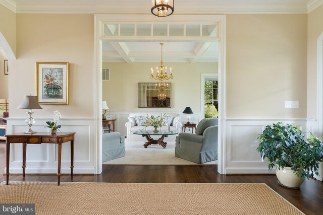 living area with a chandelier, coffered ceiling, wood finished floors, beamed ceiling, and a decorative wall